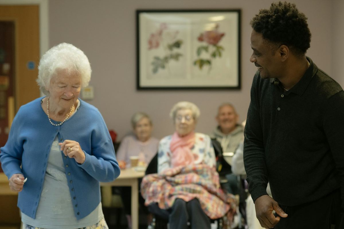 A caregiver dancing with an older woman in a bright community room